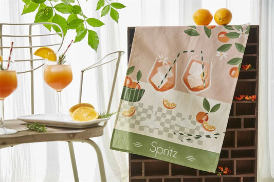 Kökshandduk i linne och bomull med motiv av Aperol Spritz-drinkar och frukter på ett bord.