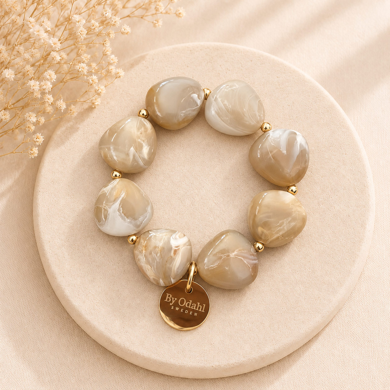 Beige marmorerat statementarmband med stora oregelbundna pärlor och guldfärgade detaljer.