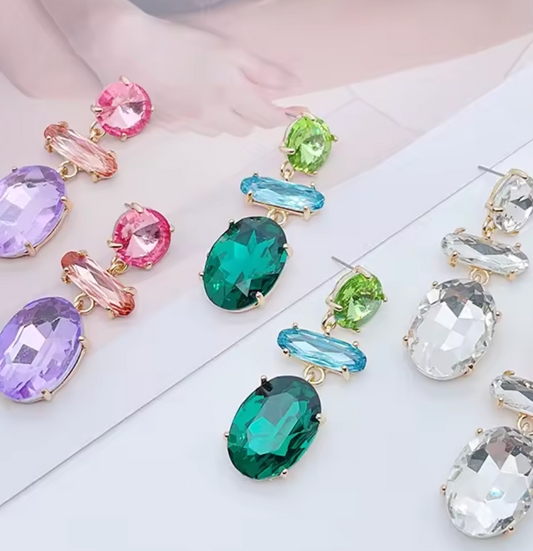 Hängande örhängen med slipade kristaller i flera färger, fotograferade mot ljus bakgrund.