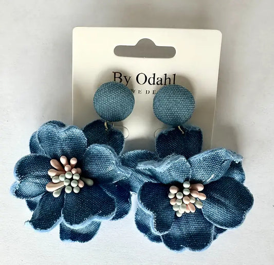 Blå blomörhängen i textil med rund överdel och dekorativ mitt, presenterade på smyckeskort.