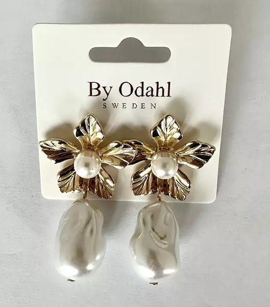 Guldtonade örhängen med dekorativa blad och vit pärldroppe, presenterade på ett smyckeskort.