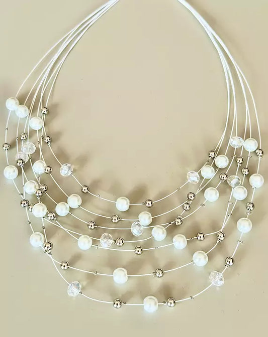 Vitt pärlhalsband med flera rader, liggande på beige bakgrund