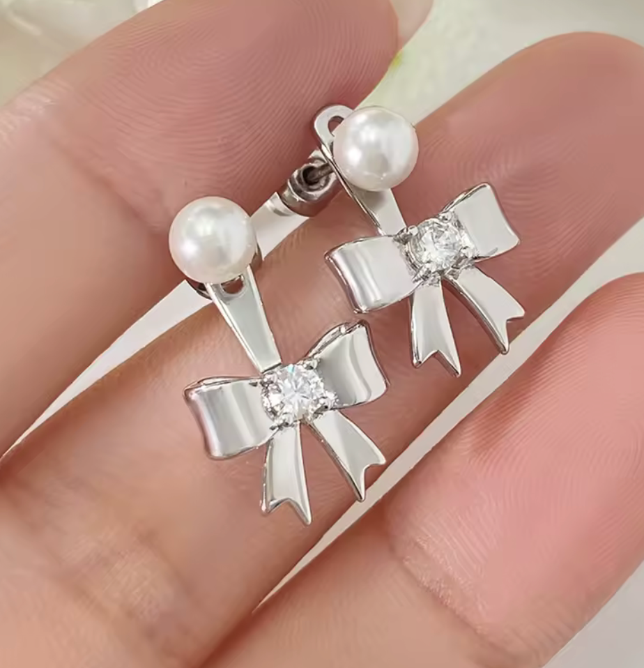 Örhängen i form av en rosett med liten pärla och zirkonsten, tillverkade i silverfärgad plätering.