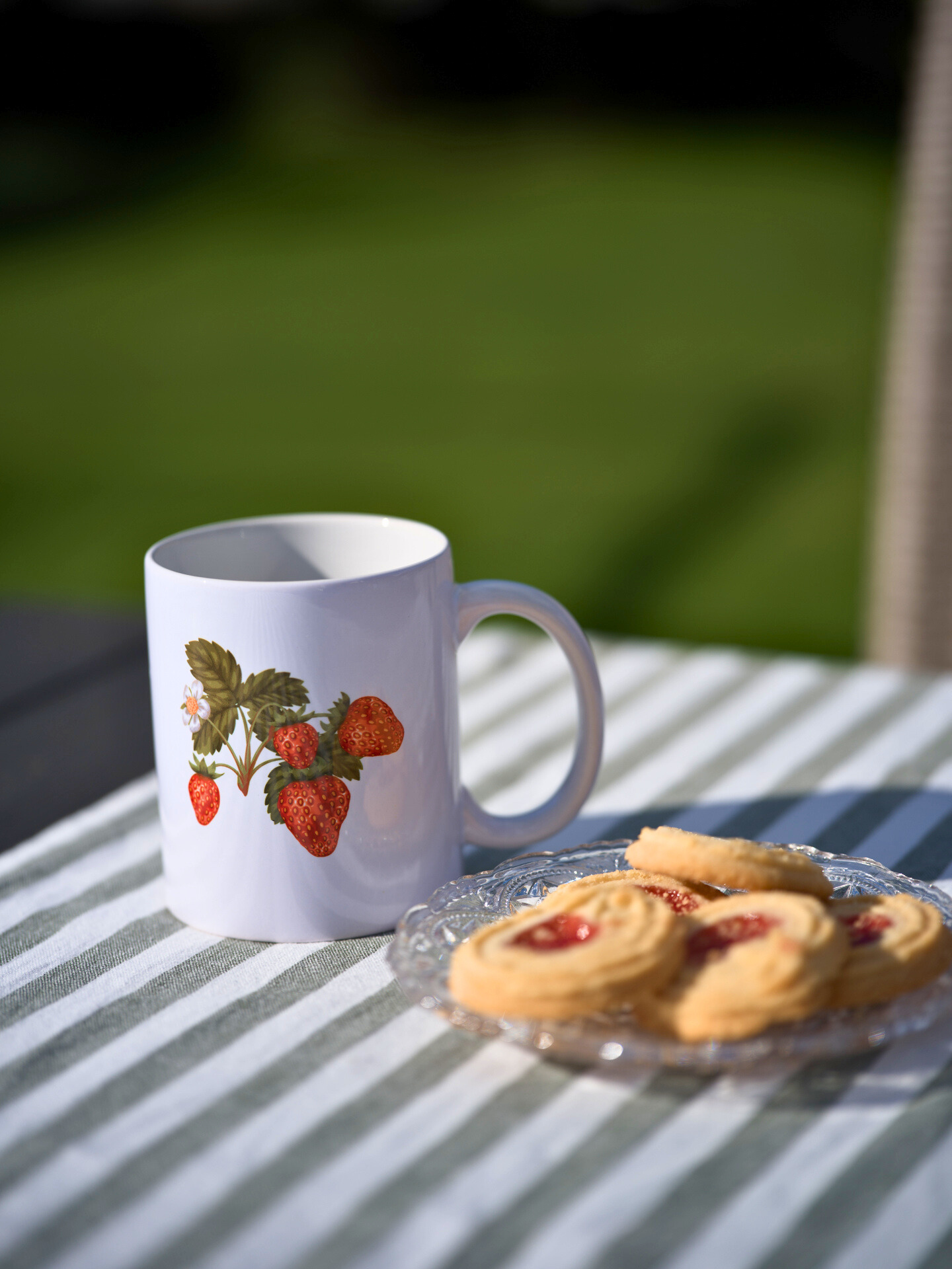 Vit mugg med jordgubbsmotiv på bord med fika