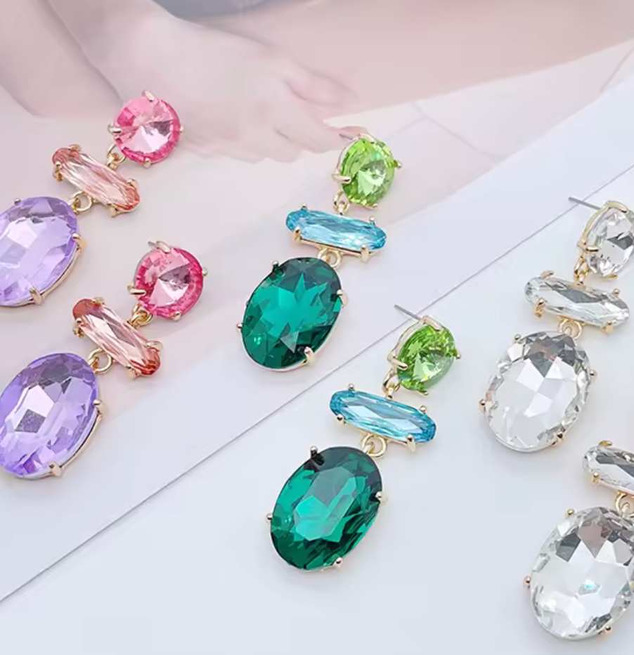 Hängande örhängen med slipade kristaller i flera färger, fotograferade mot ljus bakgrund.