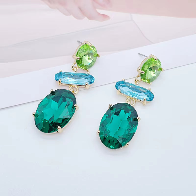Kristallörhängen i gröna och blå toner med guldfärgad infattning.