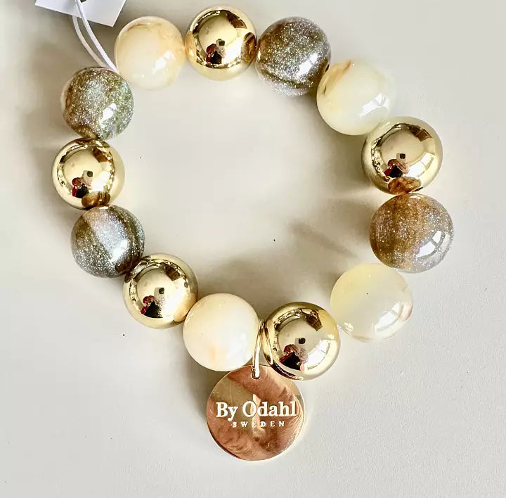 Elastiskt armband från By Odahl med pärlor i champagnefärgade toner och gulddetaljer.