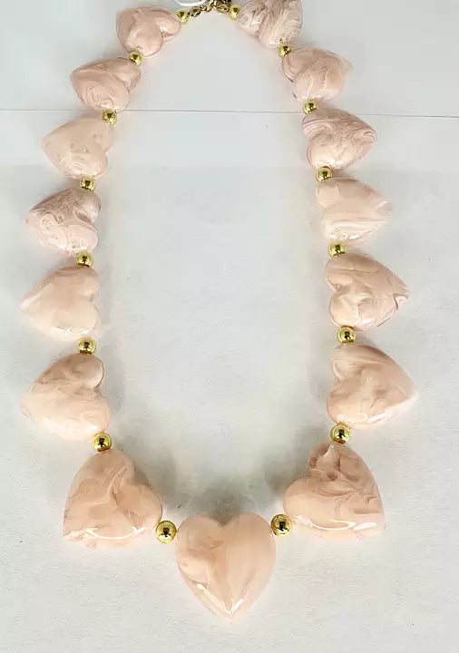 Halsband med ljusrosa hjärtformade pärlor och guldfärgade mellandetaljer på ljus bakgrund.