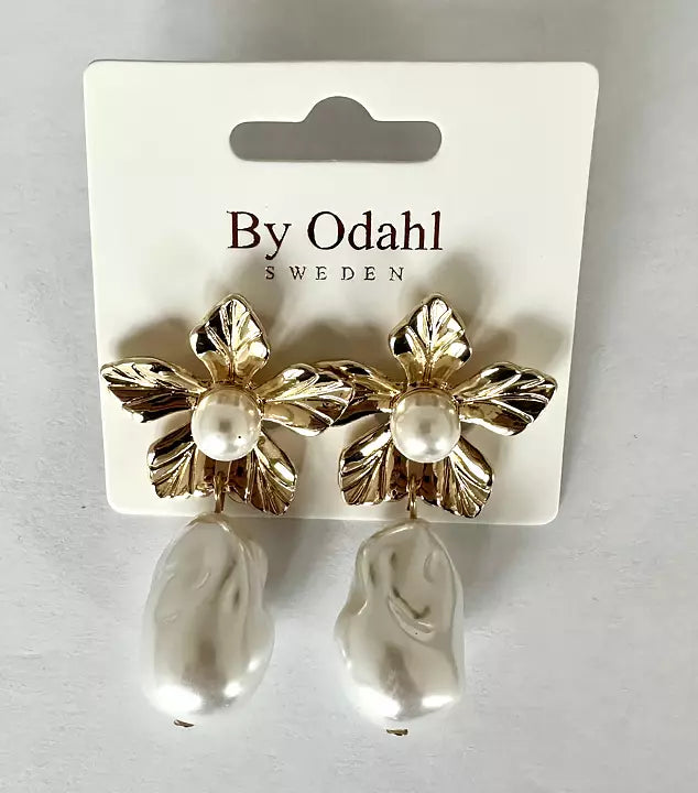 Guldtonade örhängen med dekorativa blad och vit pärldroppe, presenterade på ett smyckeskort.