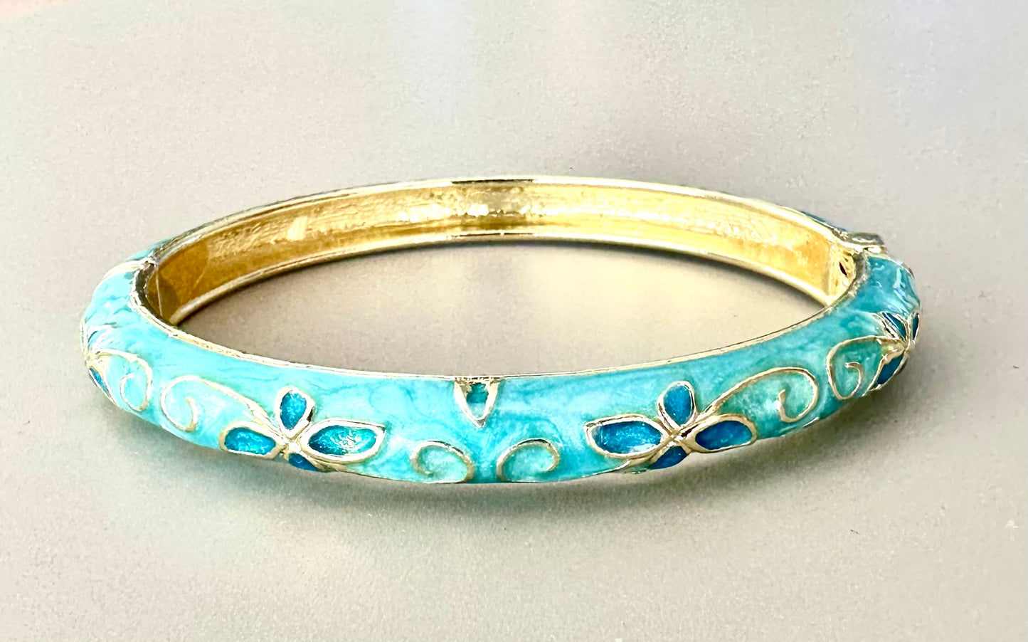 Blått Emaljerat armband med dekorativa blomdetaljer och guldfärgad insida.