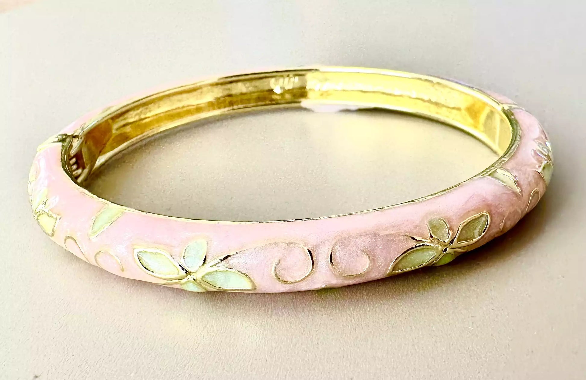 Emaljerat armband med dekorativa blomdetaljer och guldfärgad insida.