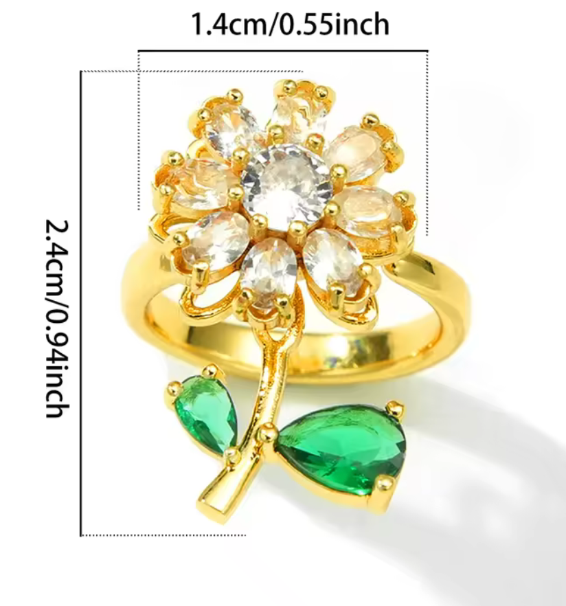 Guldpläterad justerbar ring med blomma av klara zirkonstenar och två gröna droppformade gröna stenar som blad. Toppen är snurrbar.